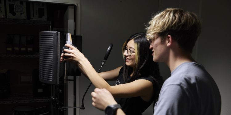 Two students set up a microphone in a recording studio