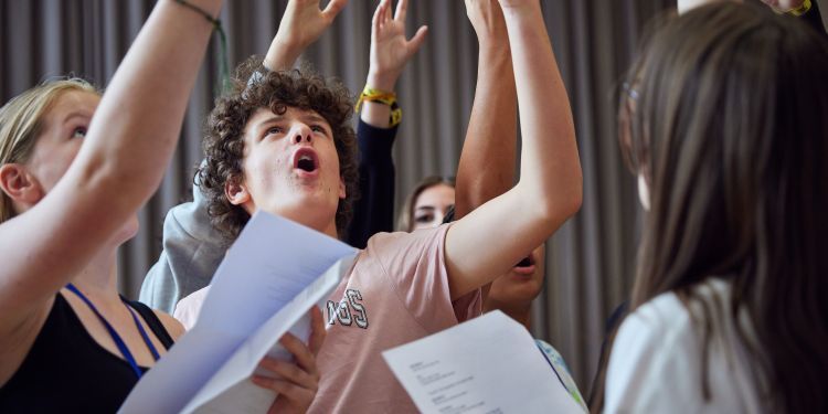 A group of young actors holding scripts, one hand dramatically raised aloft.