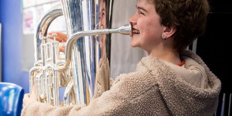 Student with beige fluffy hooded top playing euphonium