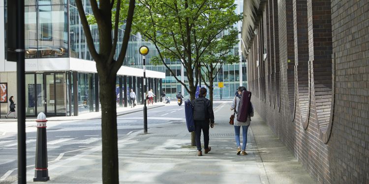 Two students with instruments walking down Silk Street on a sunny day