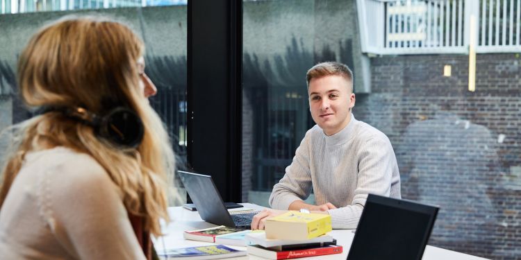 Man and woman on opposite sides of desk with laptops and books