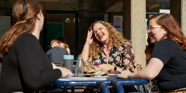 Students chatting at a bench table on lakeside terrace on a sunny day