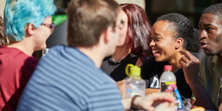 Students sat at a table chatting on lakeside terrace on a sunny day