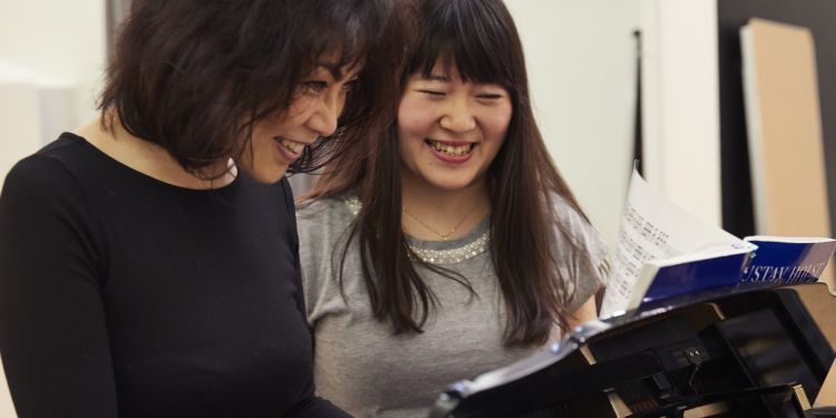 Teacher and student standing at a piano and smiling