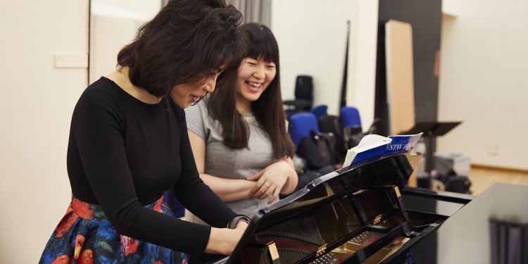 Teacher and student standing at a piano and smiling