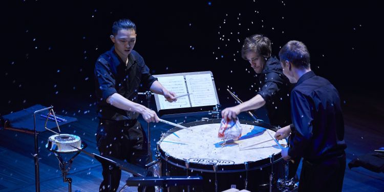 Three percussionists performing around the same drum