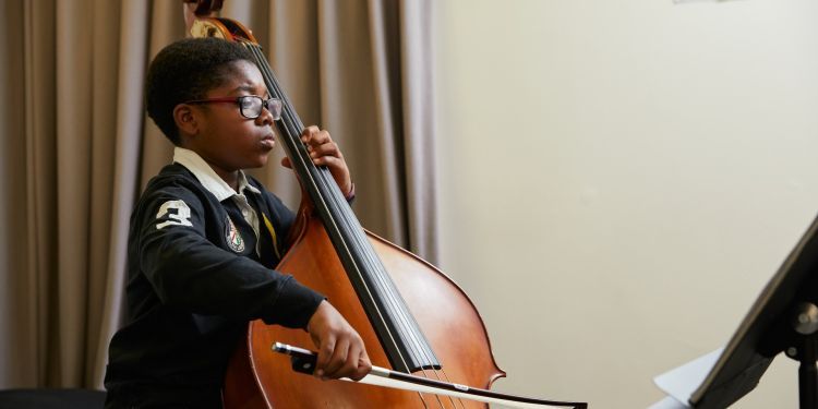 A boy with black hair and wearing a black long sleeved top plays the violin