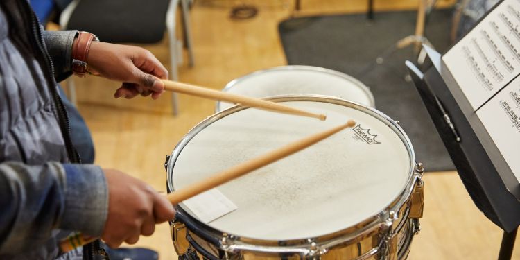 A close up image of some hands holding drum sticks over a drum kit.