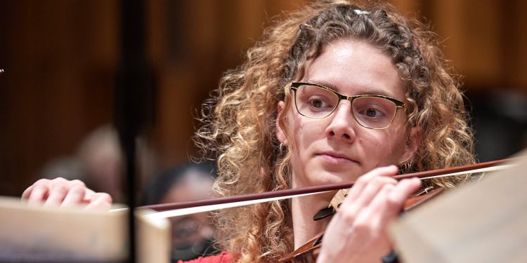 Violinist sitting straight with bow across the violin in a rehearsal