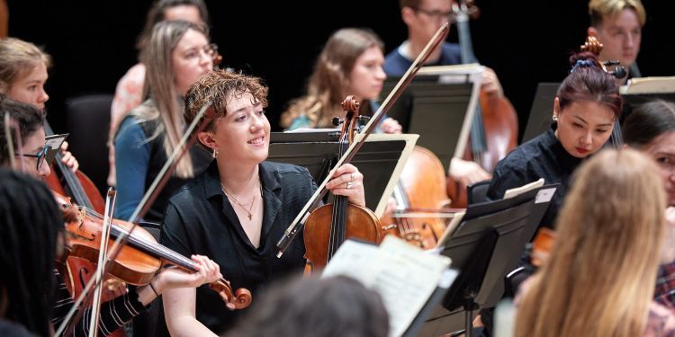 Strings players look up at the conductor during a rehearsal