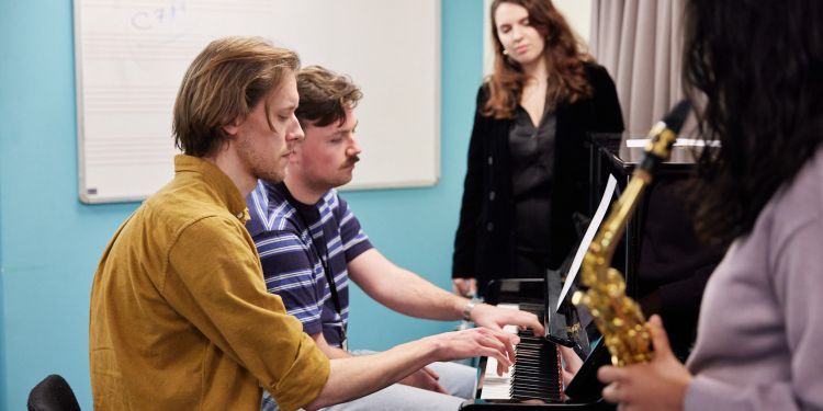 Music Therapy students in a class around a piano, one holding a saxophone