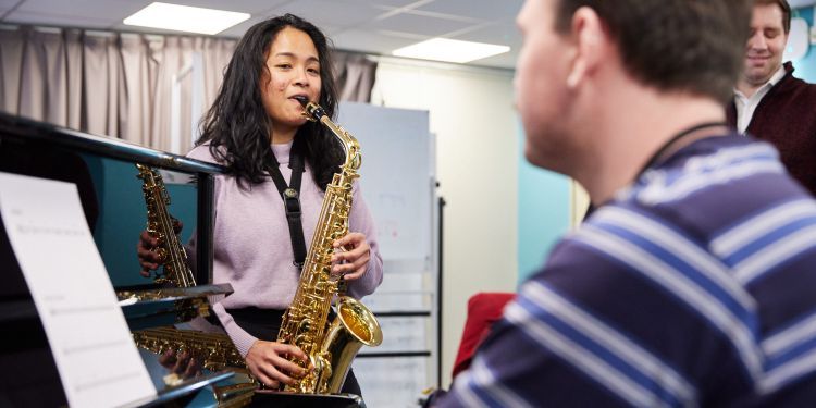 Music Therapy student in class playing piano and saxophone