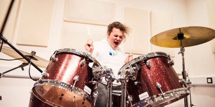 A wearing a white jumper play a red glittery drum kit