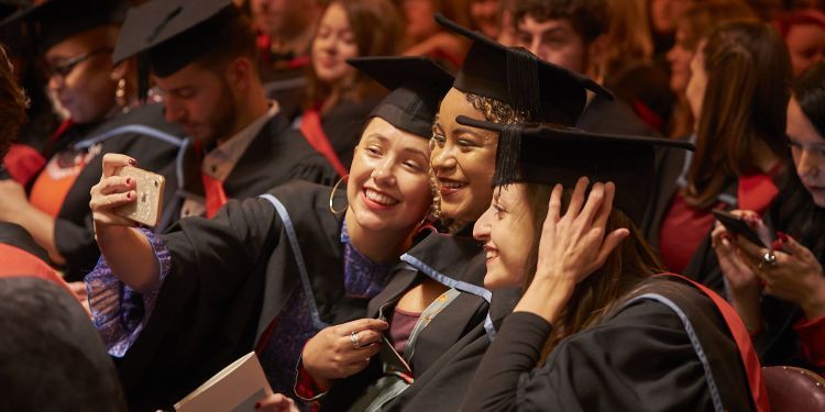 Three students in graduation gowns take a selfie in their seats