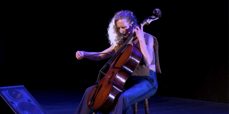 A white woman with blonde hair plays the cello