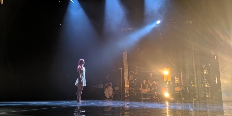 Student stands on the theatre stage under blue and yellow lighting