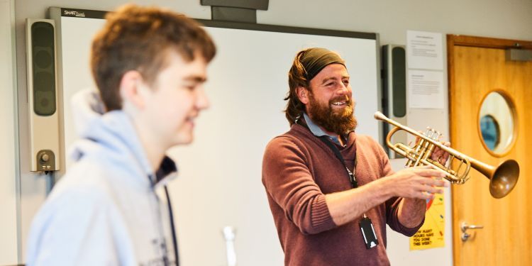 A man wears a red jumper and holds a trumpet