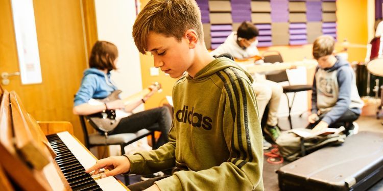 A young boy in a green jumper with adidas written across the front plays the piano