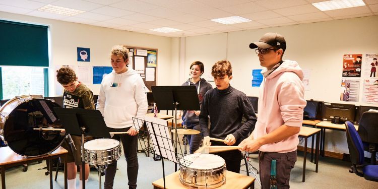 Four students play the drums with their tutor 