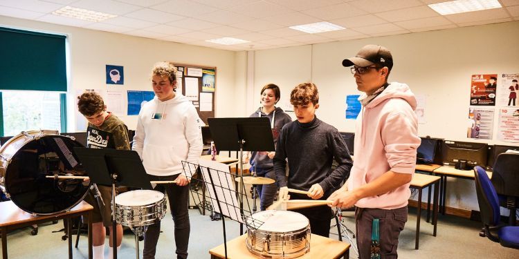 Four students play the drums with their tutor