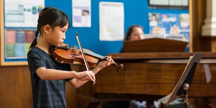 Girl in checked dress having a violin lesson with tutor on grand piano