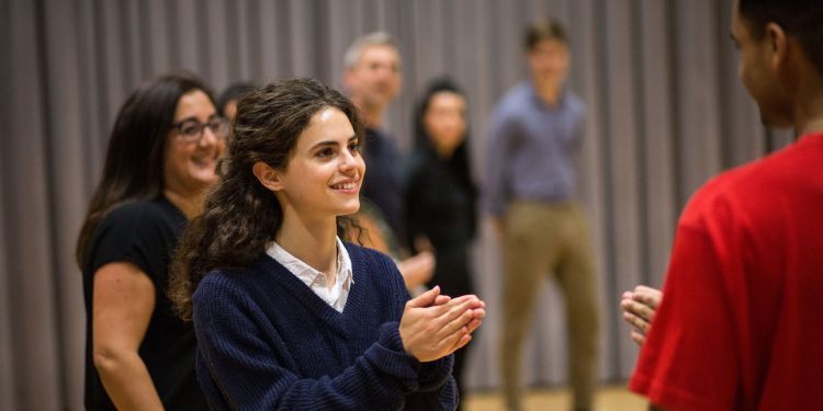 A girl wearing a blue jumper holds her hands in front of her. She has a smile on her face.