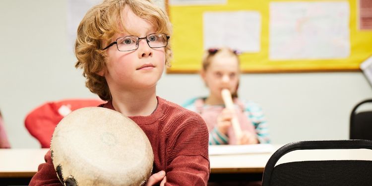 A boy in a red jumper holds a drum