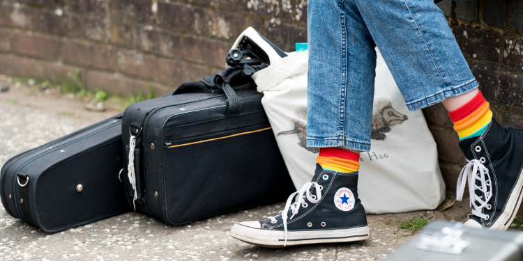 A pair of legs wearing stripy rainbow coloured socks and converse shoes 