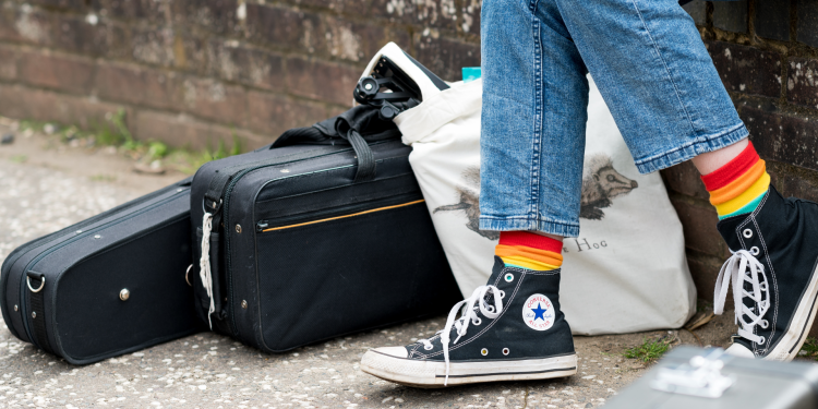 A pair of legs wearing stripy rainbow coloured socks and converse shoes
