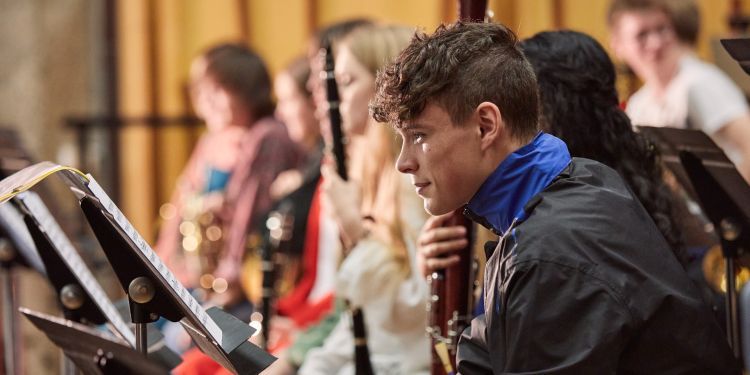 A boy wearing a blue neckerchief sits with his bassoon 