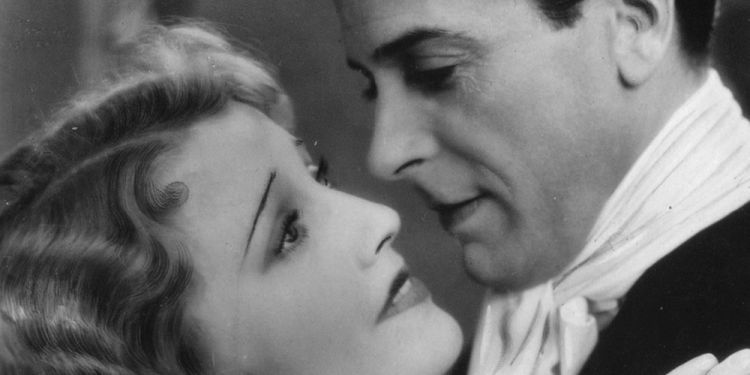 Black and white still of a woman and man looking at each other, faces nearly touching