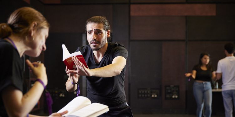 A man holds a text infront of him, his arm is out