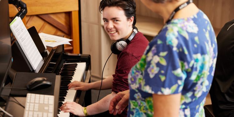 A young man at a keyboard smiling at the teacher.