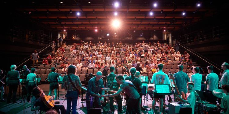 A shot of a large group of musicians on stage, taken looking out over the audience