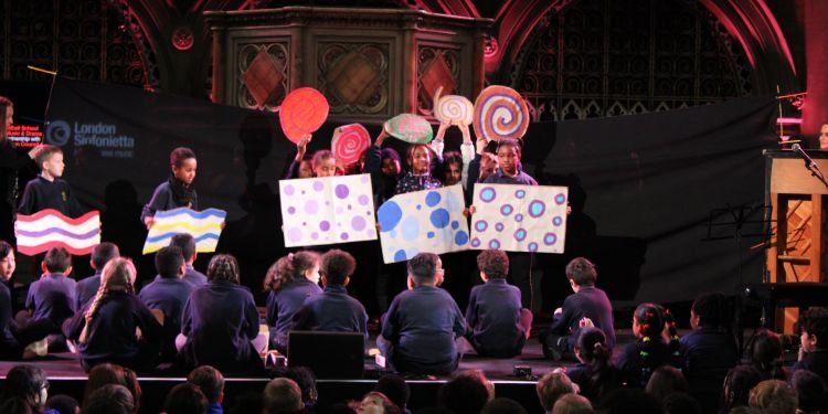 A group of children on stage holding up colourful signs and pictures as part of a musical performance