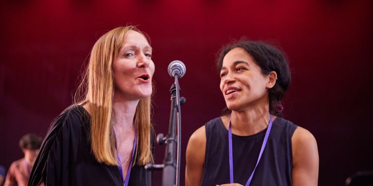Two women sharing a microphone, smiling and singing together
