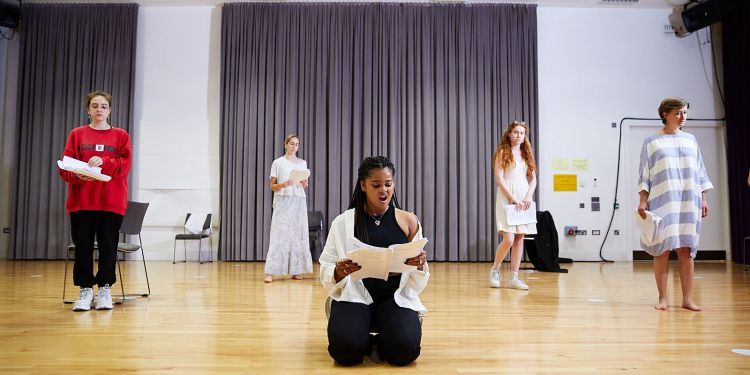 participants rehearsing in a room standing and one participant sitting holding a script