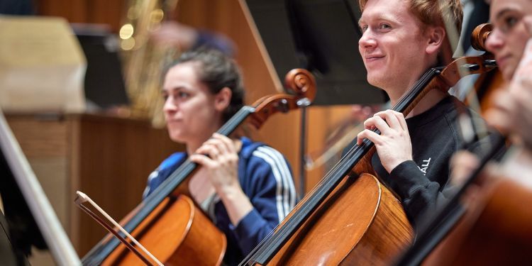 Male and female student sat next to each other with their string instrument
