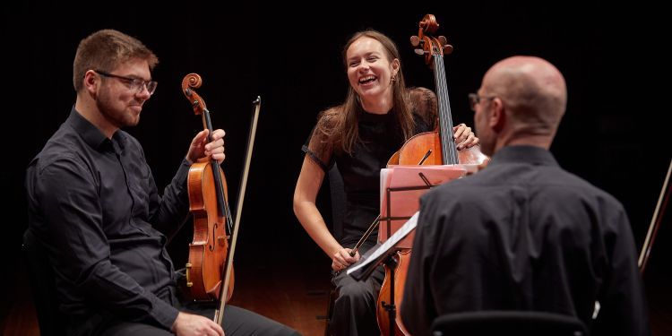 Three chamber students sat laughing holding onto their instruments