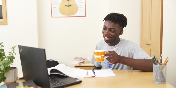 A boy sits at a desk, holding an orange mug 