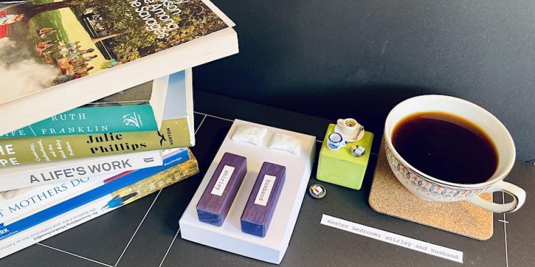 Photo of a desk set up featuring many books, and a cup of tea and a model or a bedroom design
