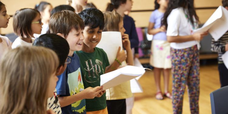 Three boys laugh whilst holding out a song sheet 