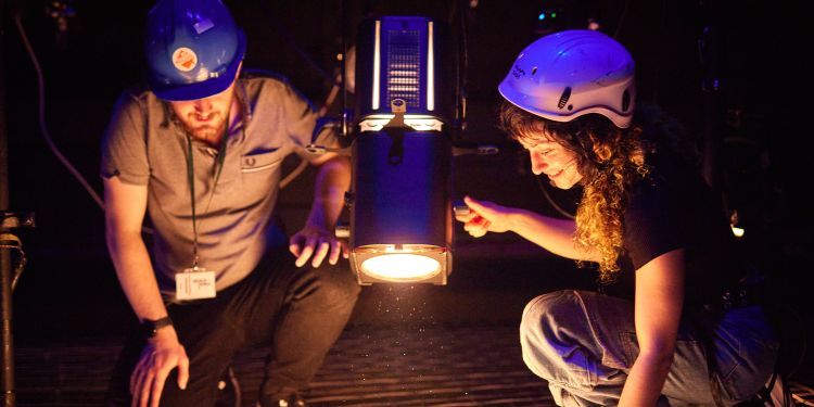 Image of two people wearing helmets using light above stage
