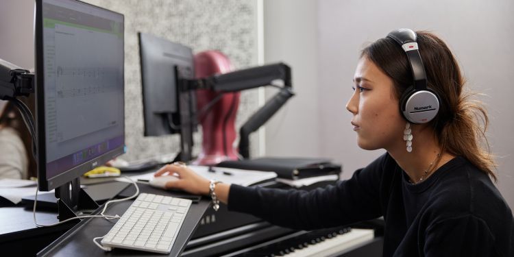 Image of woman with headphones in looking at a computer screen with her hand on the mouse