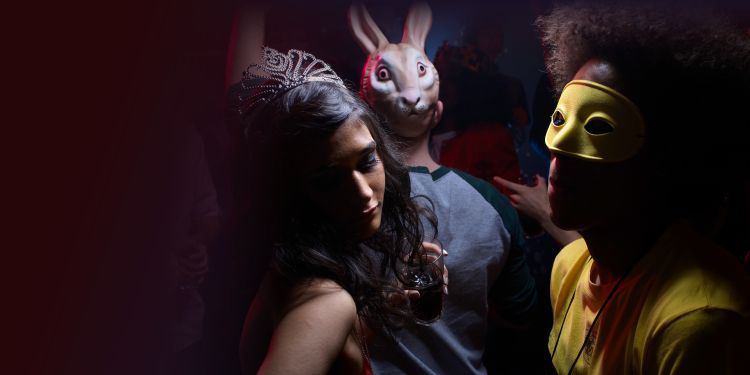 Party scene with person on left wearing a tiara and holding drink, person in middle with rabbit mask on face, person on right with yellow mask over eyes