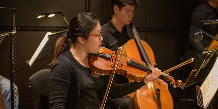 Student playing violin with another student in the background with cello