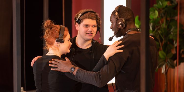 Three students with their arms around one another behind the scenes working on a student drama production 