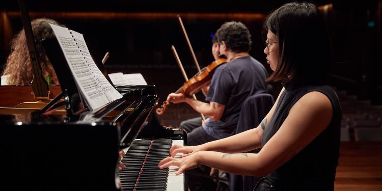 Pianist performing with two violinists in background