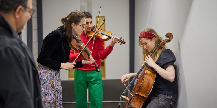 Three students tuning up their string instruments back stage