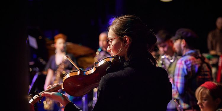Photo taken of the back of a student tuning a violin